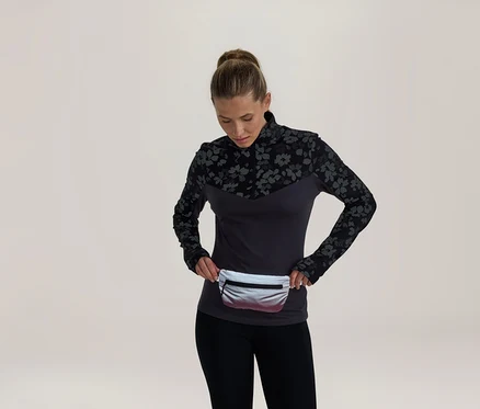 Femme portant un haut à manches longues gris foncé avec un motif floral noir sur les épaules et les manches, un legging noir et une banane argentée, regardant la banane.