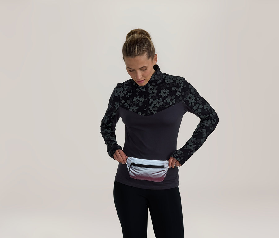 Femme portant un haut à manches longues gris foncé avec un motif floral noir sur les épaules et les manches, un legging noir et une banane argentée, regardant la banane.