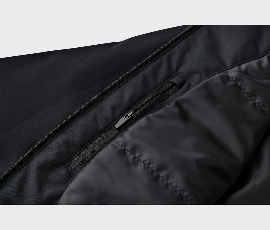 Gros plan d'une veste noire avec une fermeture éclair principale, une poche zippée partiellement ouverte et une doublure intérieure matelassée.