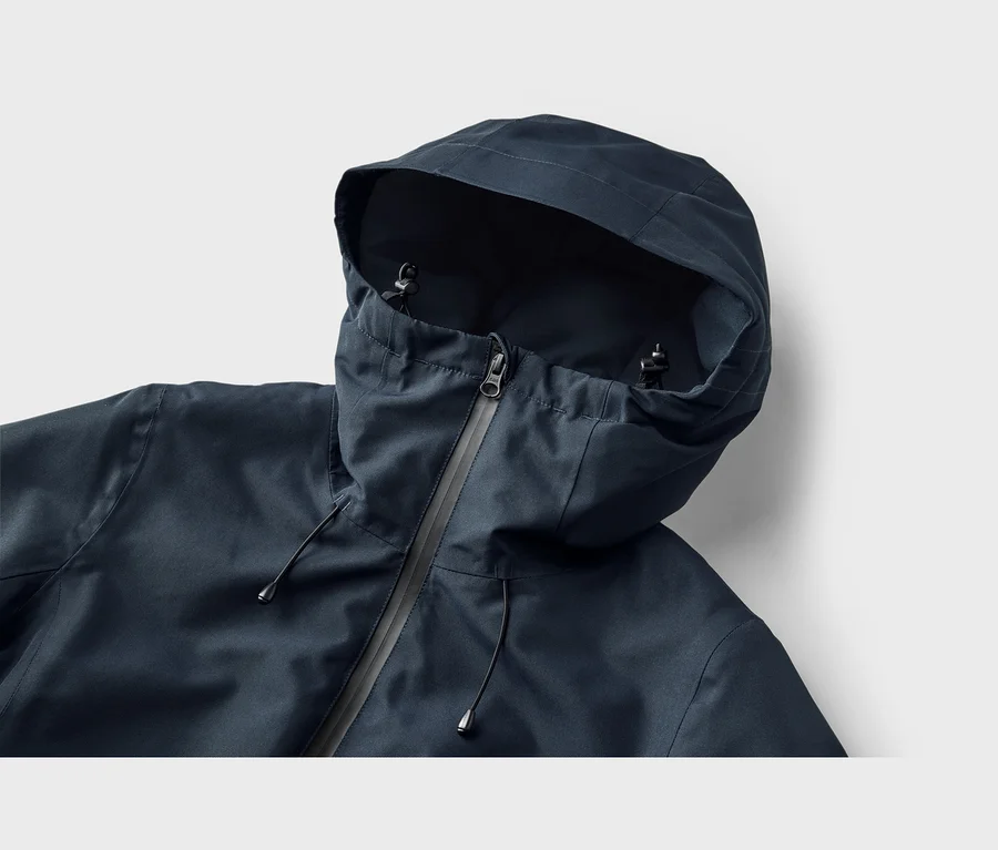 Gros plan d'une veste à capuche bleu foncé avec une fermeture éclair grise partiellement ouverte et des cordons de serrage visibles avec des stoppeurs sur la capuche.