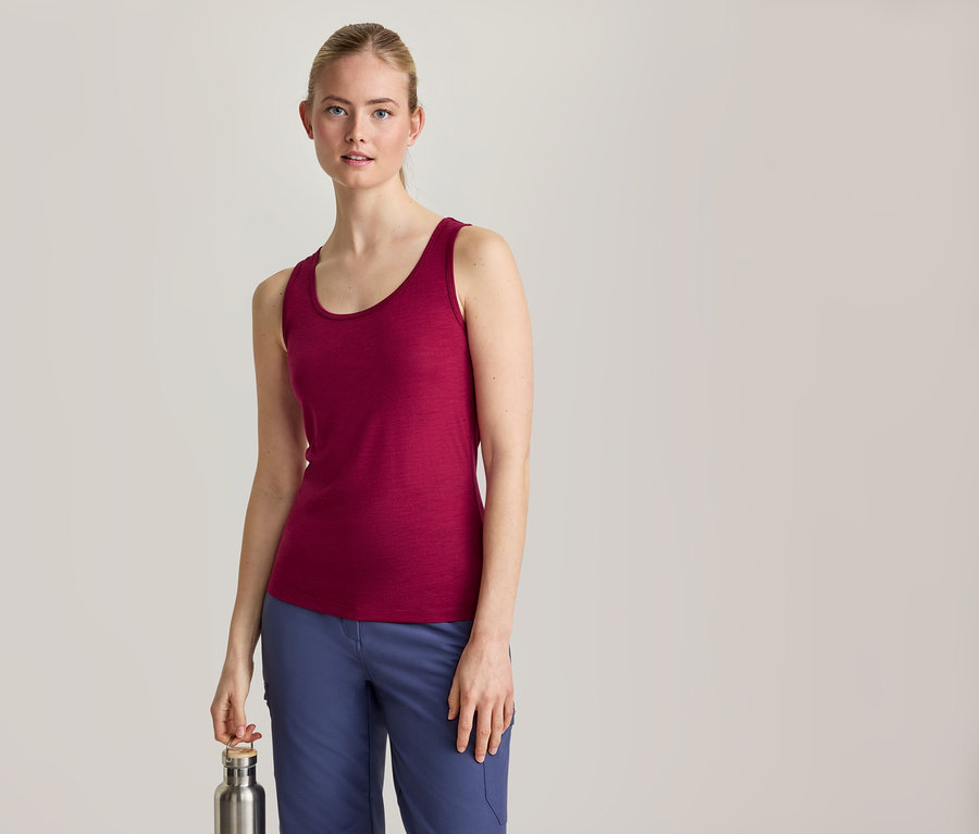 Une femme aux cheveux blonds attachés, vêtue d'un débardeur magenta et d'un pantalon bleu, se tient de face et tient une bouteille d'eau argentée dans sa main droite.