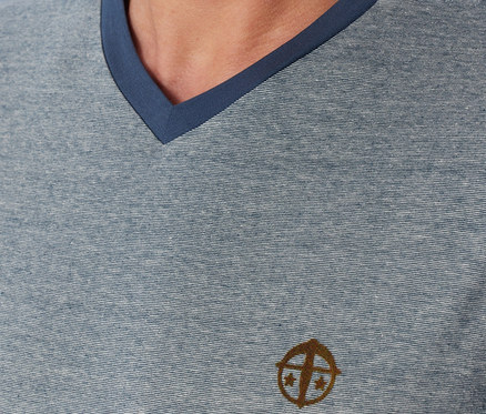 Gros plan d'un homme portant un t-shirt chiné bleu-gris à col en V, avec un liseré bleu foncé et un logo marron sur la poitrine.