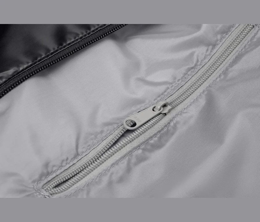 Gros plan d'un tissu gris avec une fermeture éclair grise partiellement ouverte. Un tissu noir avec une fermeture éclair noire est visible en haut à gauche.