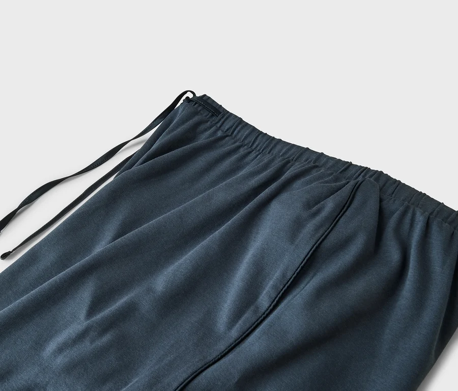 Gros plan d'un tissu bleu foncé ou gris avec une ceinture élastique et un cordon de serrage noir. Une couture verticale est visible.