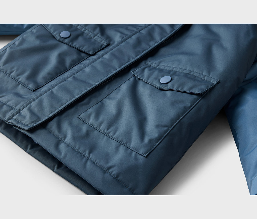 Gros plan d'une veste bleue montrant deux poches à rabat avec des boutons bleus assortis.