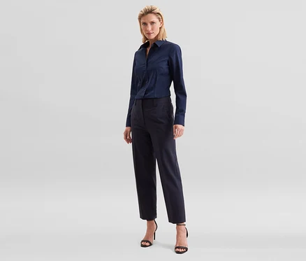 Femme blonde debout, portant une chemise à manches longues bleu marine, un pantalon cropped bleu marine et des sandales noires à talons hauts.