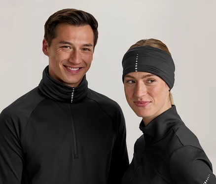 Un homme et une femme souriants portent des hauts de sport noirs à col montant avec des points réfléchissants. La femme porte également un bandeau noir avec des points réfléchissants.
