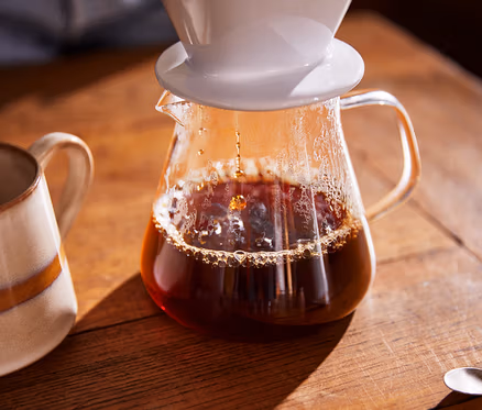Du café est versé dans une cafetière en verre, une tasse est à côté.