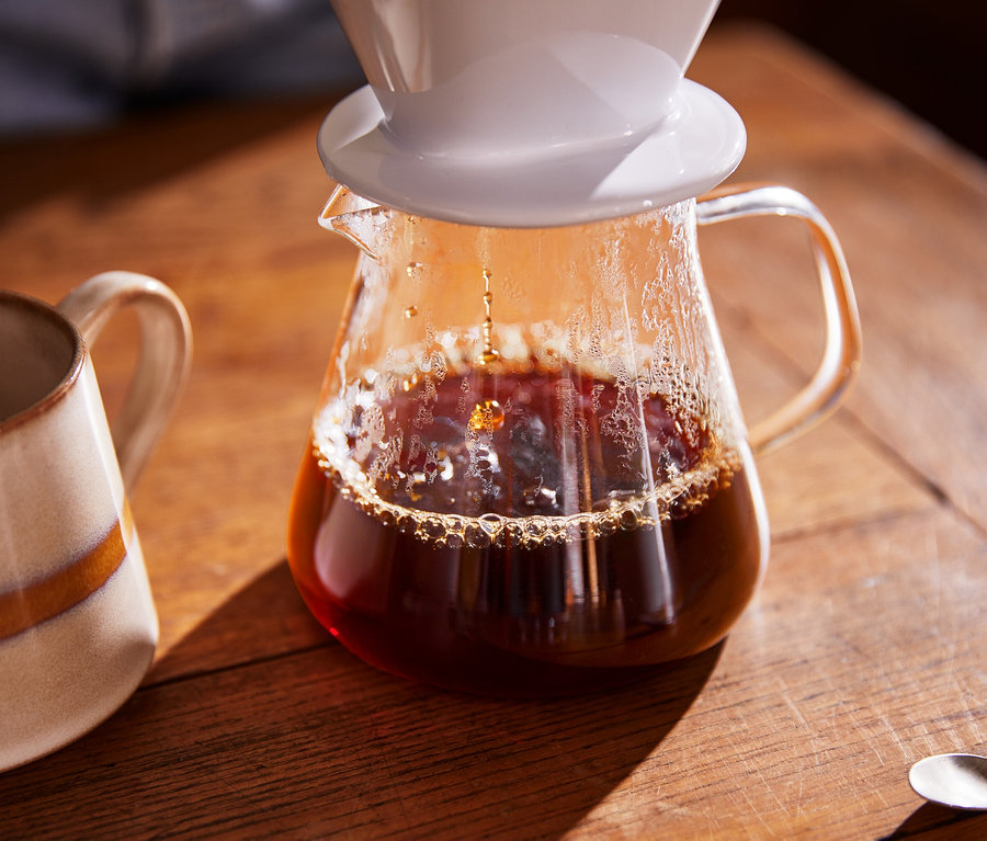 Du café est versé dans une cafetière en verre, une tasse est à côté.