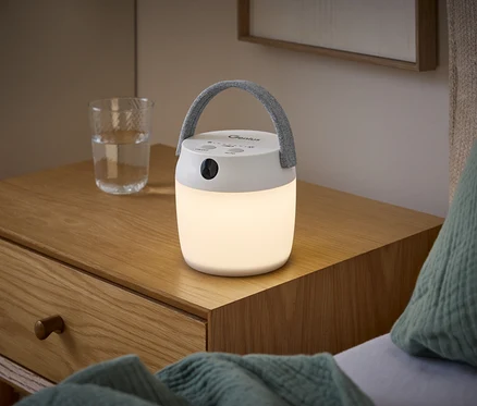 Une lampe LED multifonctionnelle avec détecteur de mouvement et poignée grise allumée sur une table de chevet en bois à côté d'un verre d'eau.