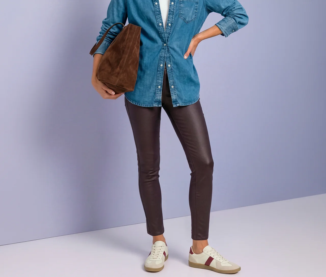 Personne portant une chemise en jean bleue, un pantalon Street One aspect cuir rouge et des baskets blanches à rayures bordeaux, tenant un sac cabas marron.