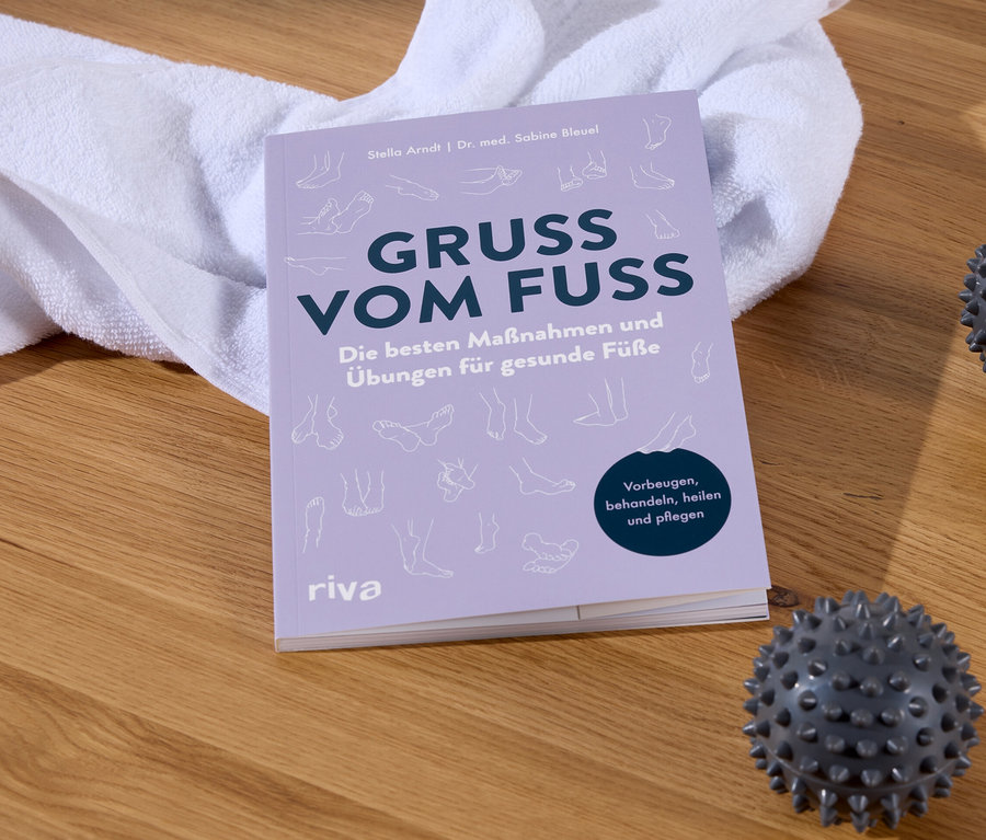 Le livre Gruss Vom Fuss à côté d'une serviette blanche et de deux balles de massage sur un plancher en bois.