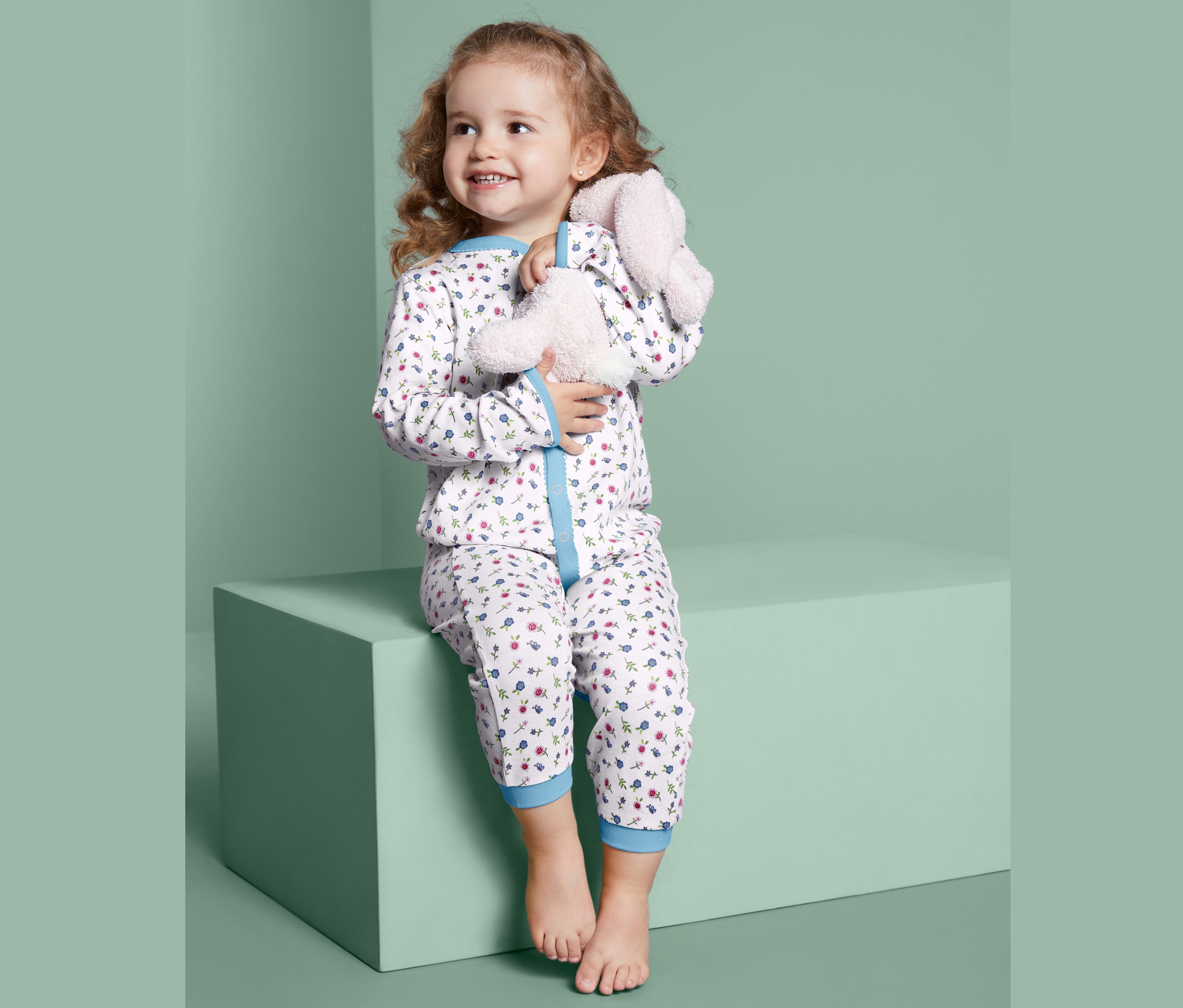 Une fille est assise sur un bloc et serre un lapin en peluche dans ses bras. Elle porte 2 pyjamas.