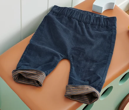 Un pantalon réversible bleu repose sur un coffre à jouets marron.