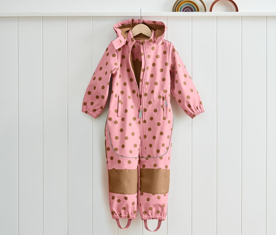 Une combinaison softshell rose à pois marron est suspendue à un cintre.