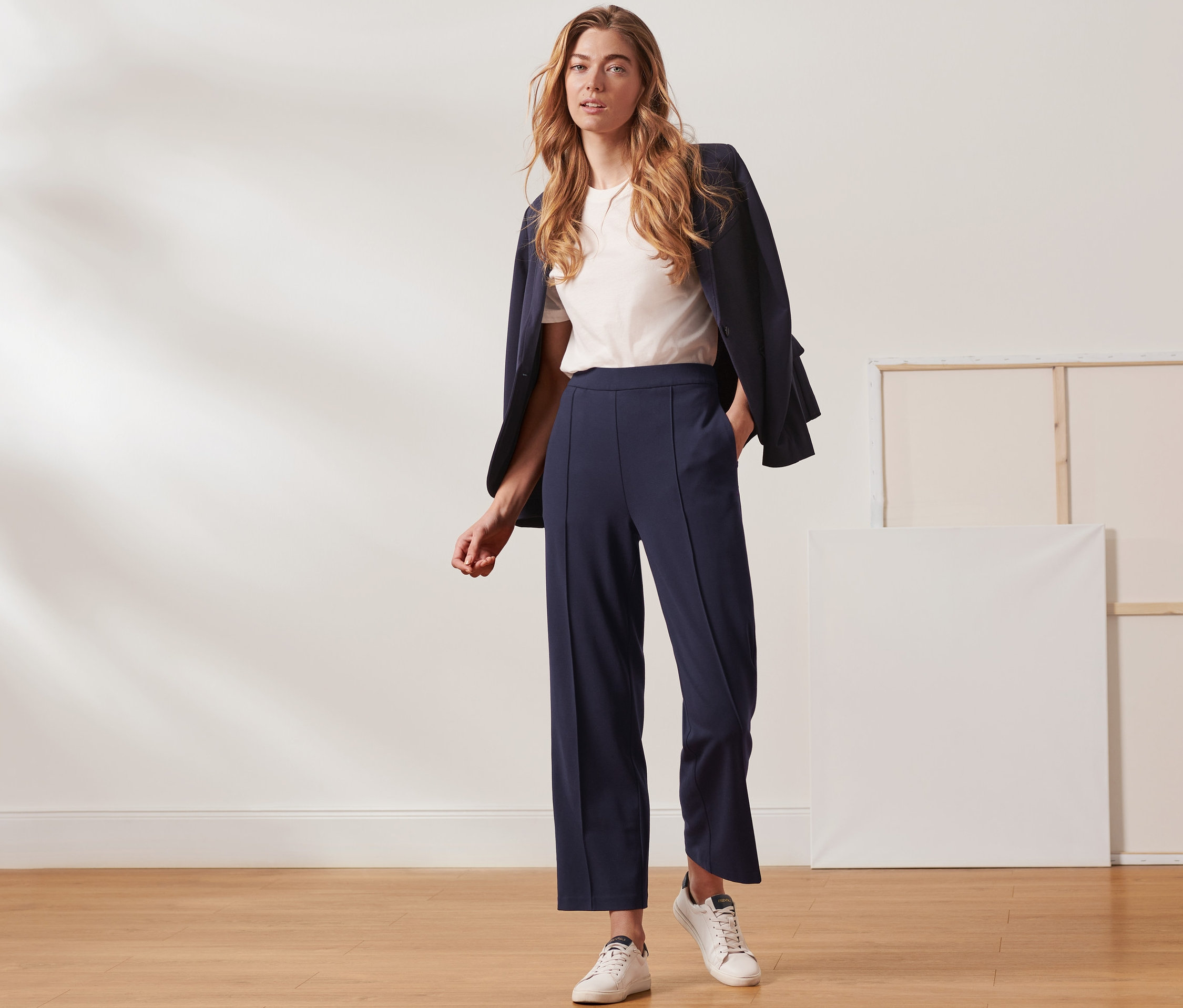 Une femme pose en studio et porte un pantalon en jersey bleu foncé avec une nervure.