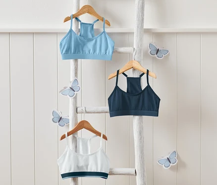 Trois brassières pour filles suspendues à des cintres sur une échelle blanche, entourées de décorations de papillons.