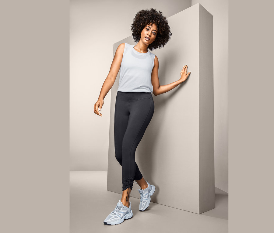 Femme posant en legging de sport 7/8, débardeur blanc et baskets.
