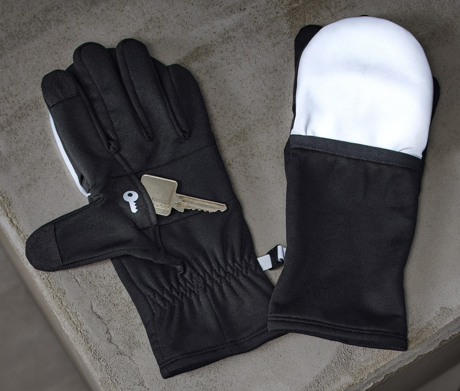 Des gants de course noirs avec rabats et une clé reposent sur une surface en béton grise à côté d'une bouteille d'eau noire.