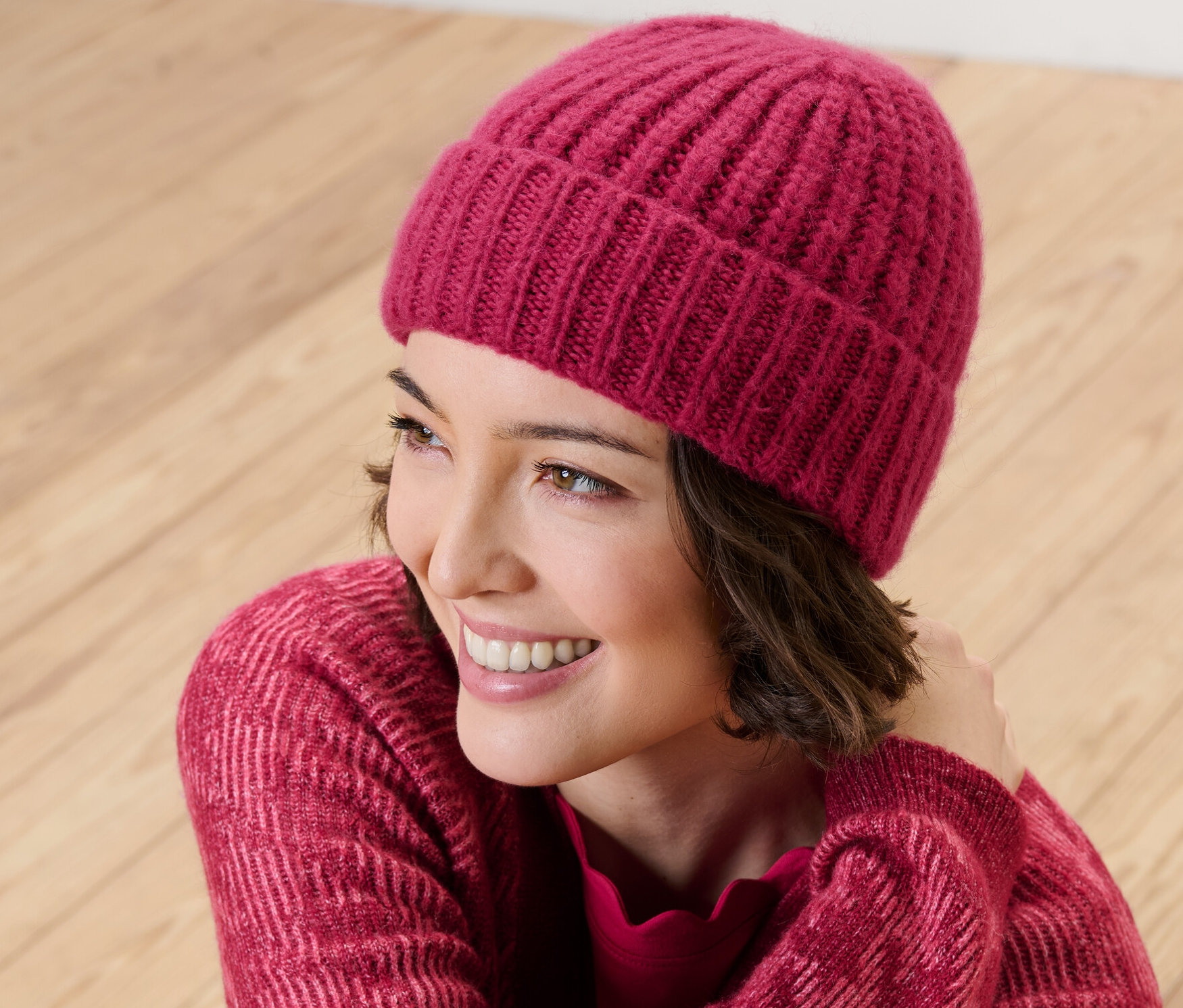 Femme souriante portant un bonnet en maille framboise.