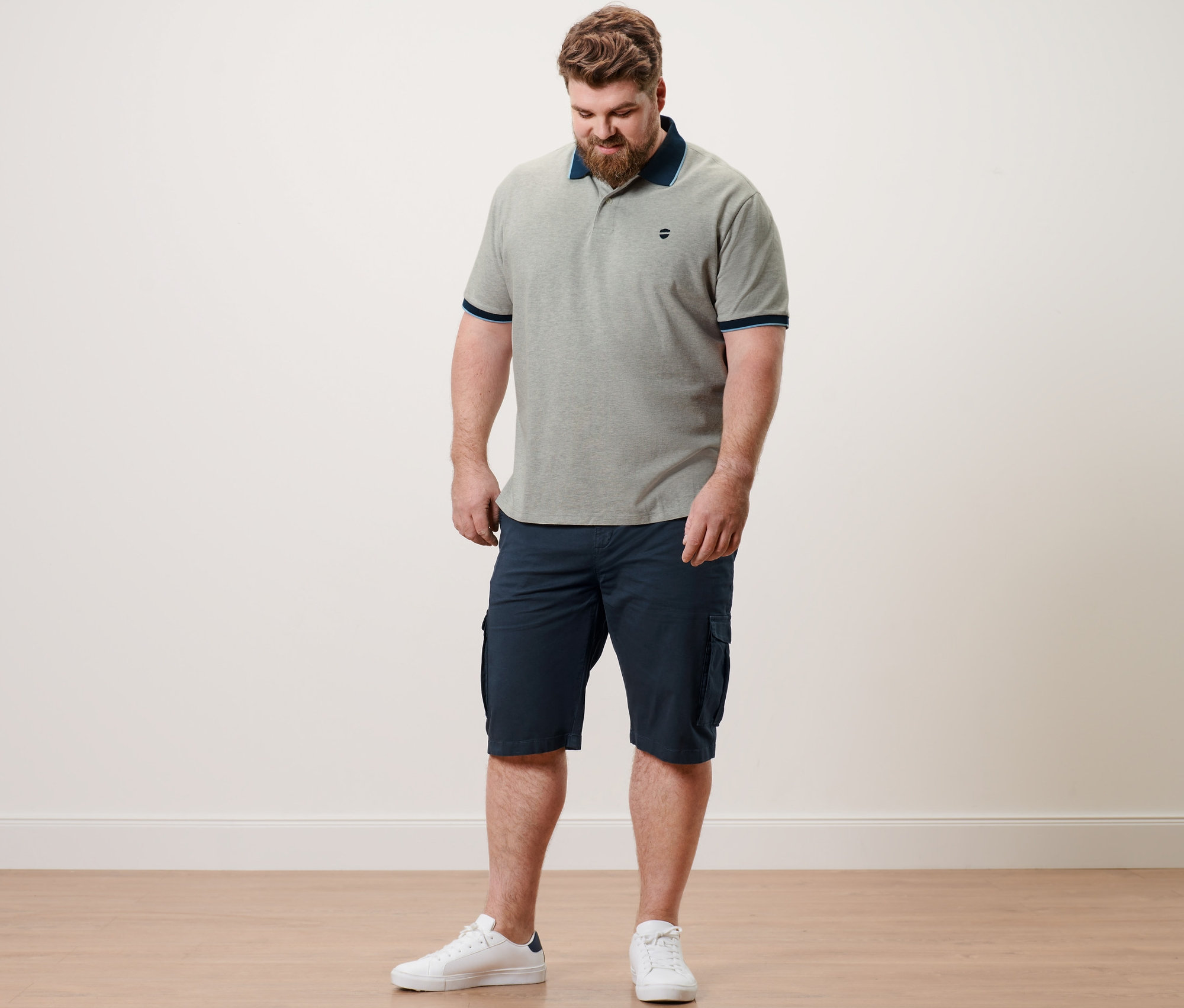 Homme portant un polo en piqué gris chiné et un short cargo bleu marine.