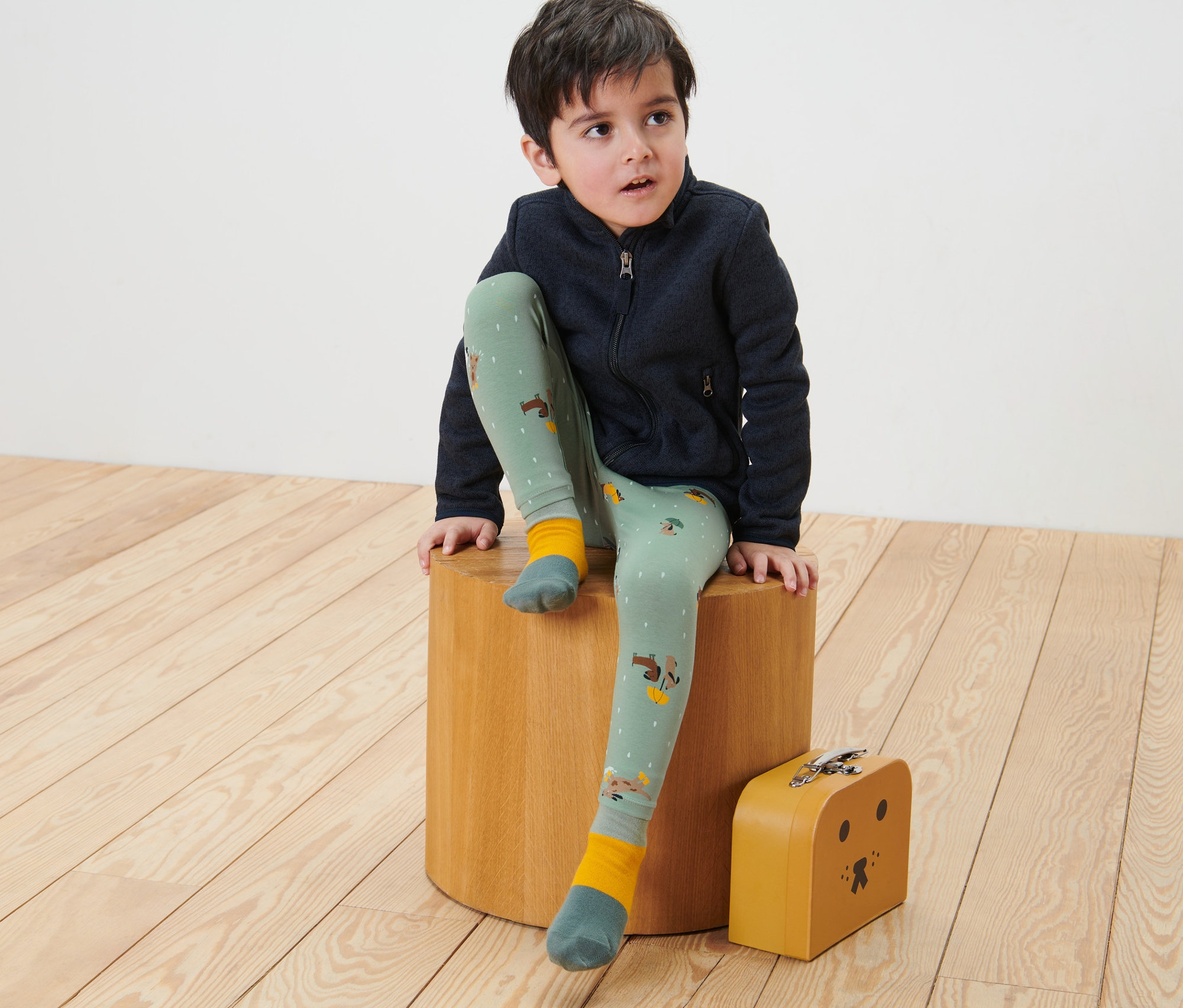 Un garçon est assis sur un tabouret en bois et porte 2 leggings pour enfant.