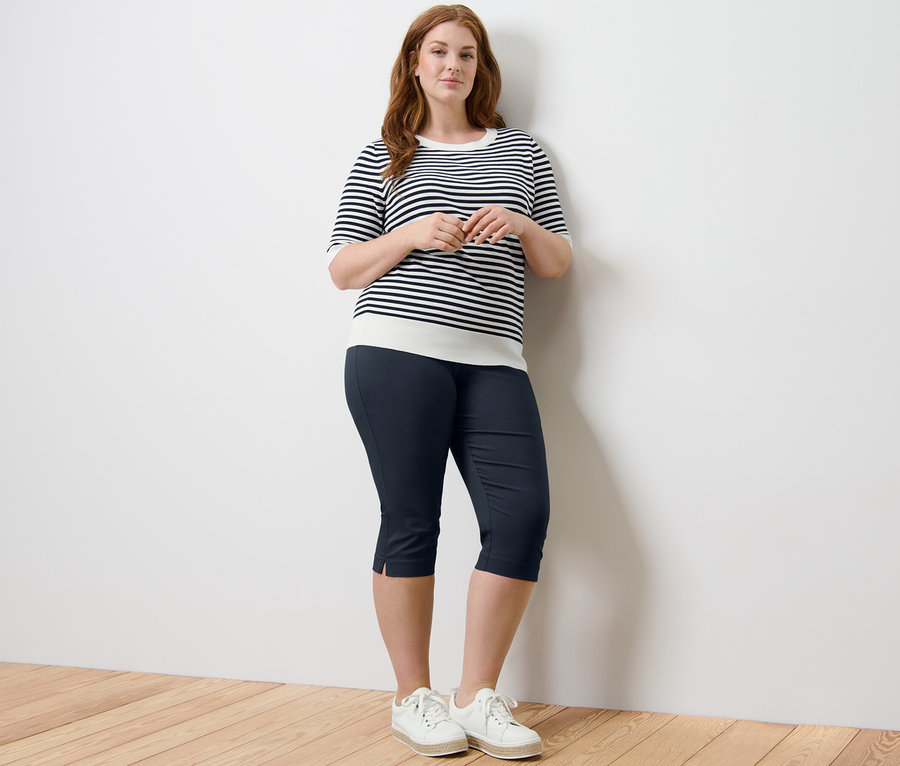 Femme posant en pull rayé en maille fine et pantalon 3/4 stretch bleu foncé.
