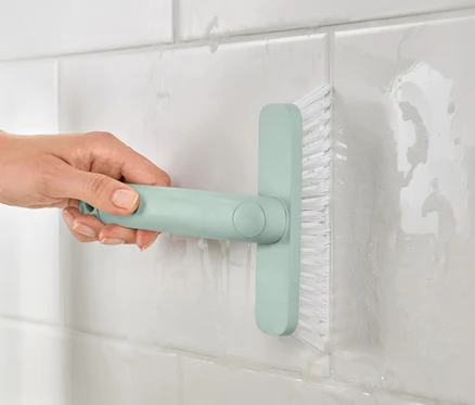 Une femme nettoie les joints de carrelage avec l'outil pour joints 4 en 1.