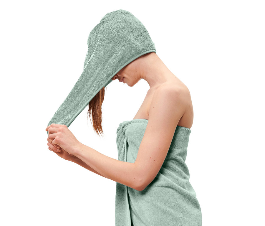 Une femme met une serviette turban bleu clair sur sa tête et a une serviette bleu clair enroulée autour de son corps.