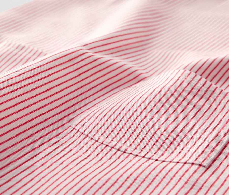 Gros plan d'une robe-salopette tissée pour enfant avec des rayures rouges et une poche.