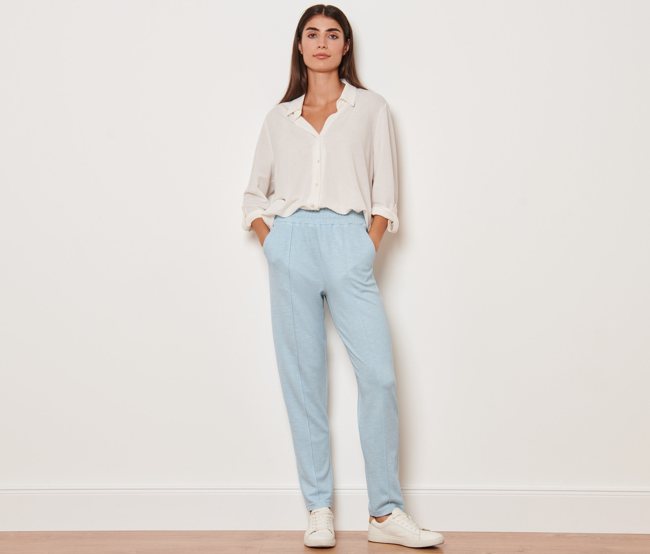 Une femme debout, les mains dans les poches de son pantalon de jogging avec nervure.