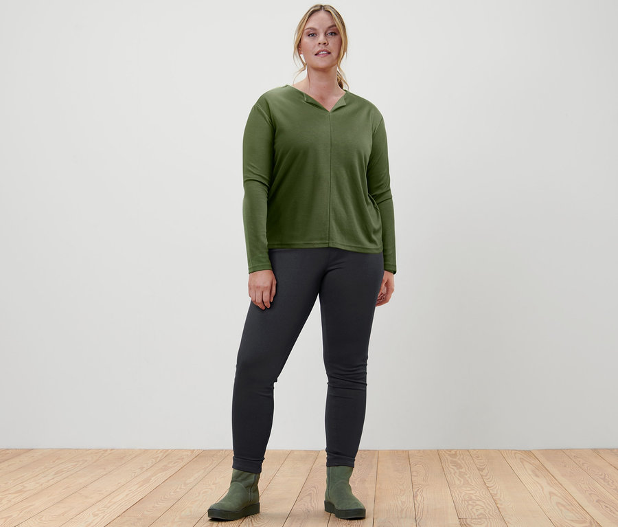 Une femme debout porte une blouse, un jegging et des bottines en cuir velours.