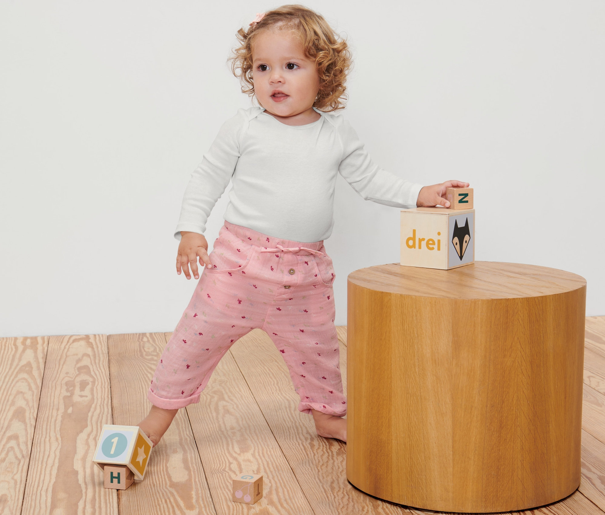 Un bébé joue avec des cubes sur un plancher en bois et porte un pantalon à enfiler pour bébé.