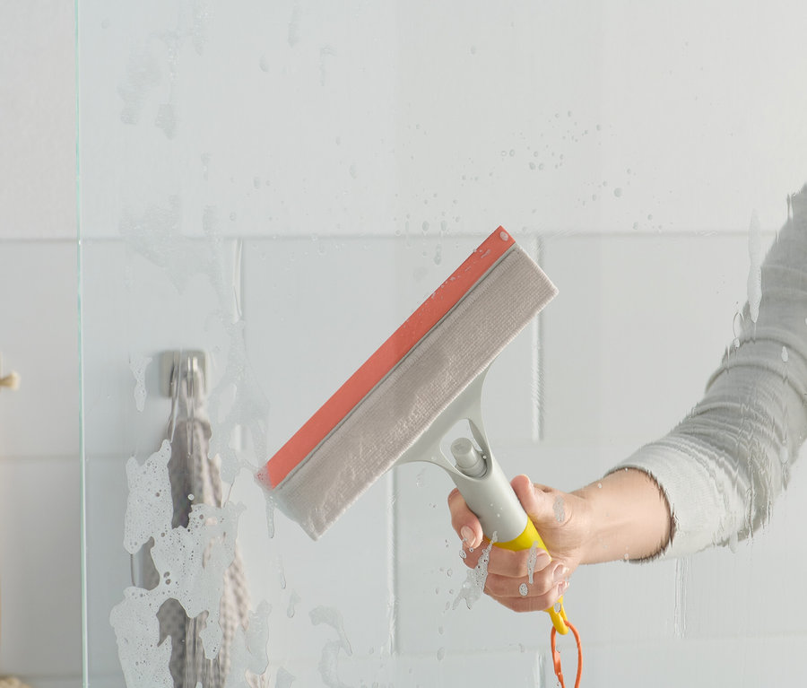 Une femme utilise une raclette 3 en 1 sur une paroi de douche en verre.