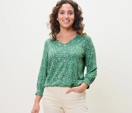 Femme posant dans une blouse imprimée verte.
