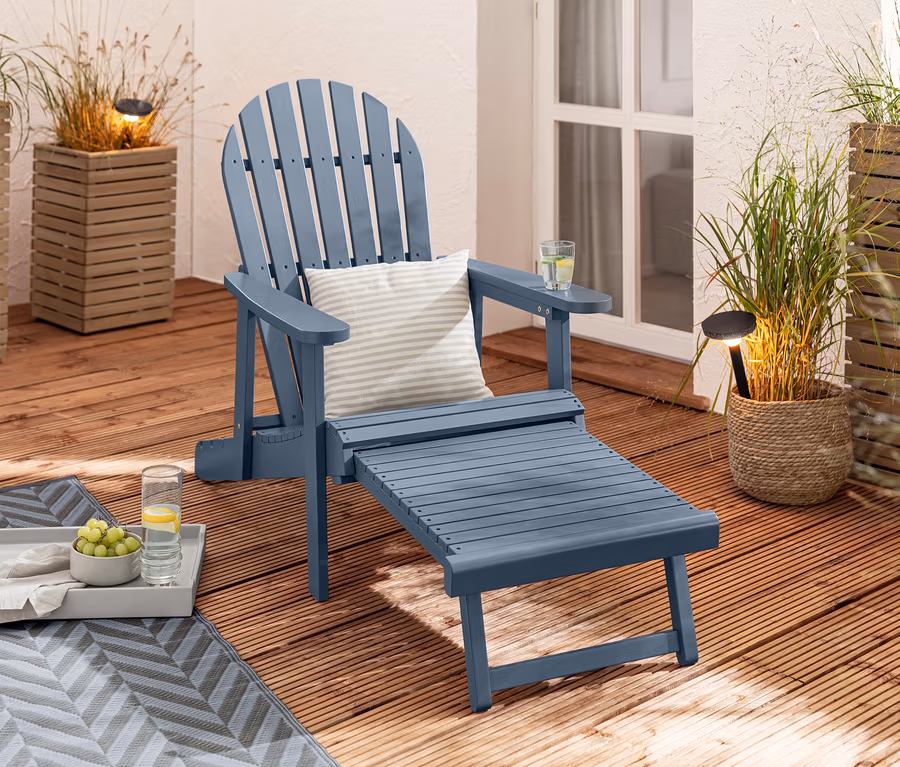 Un fauteuil de relaxation Adirondack bleu avec repose-pieds extensible est installé sur une terrasse en bois à côté de 2 lampes solaires et de 2 coussins d’extérieur en lin haptique.
