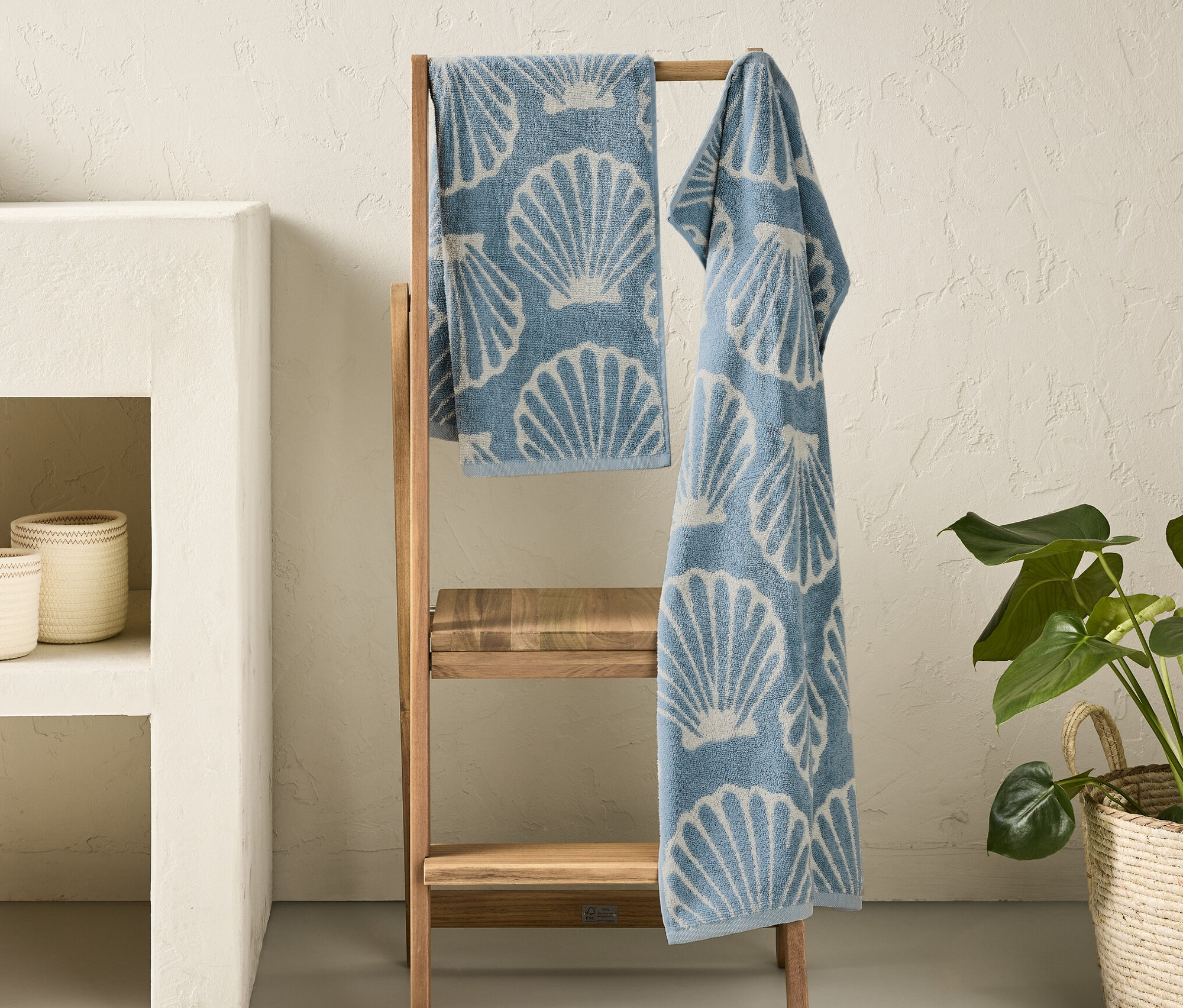 Deux serviettes bleues « Coquillage » avec imprimé de coquillages suspendues à une échelle en bois dans une salle de bain.