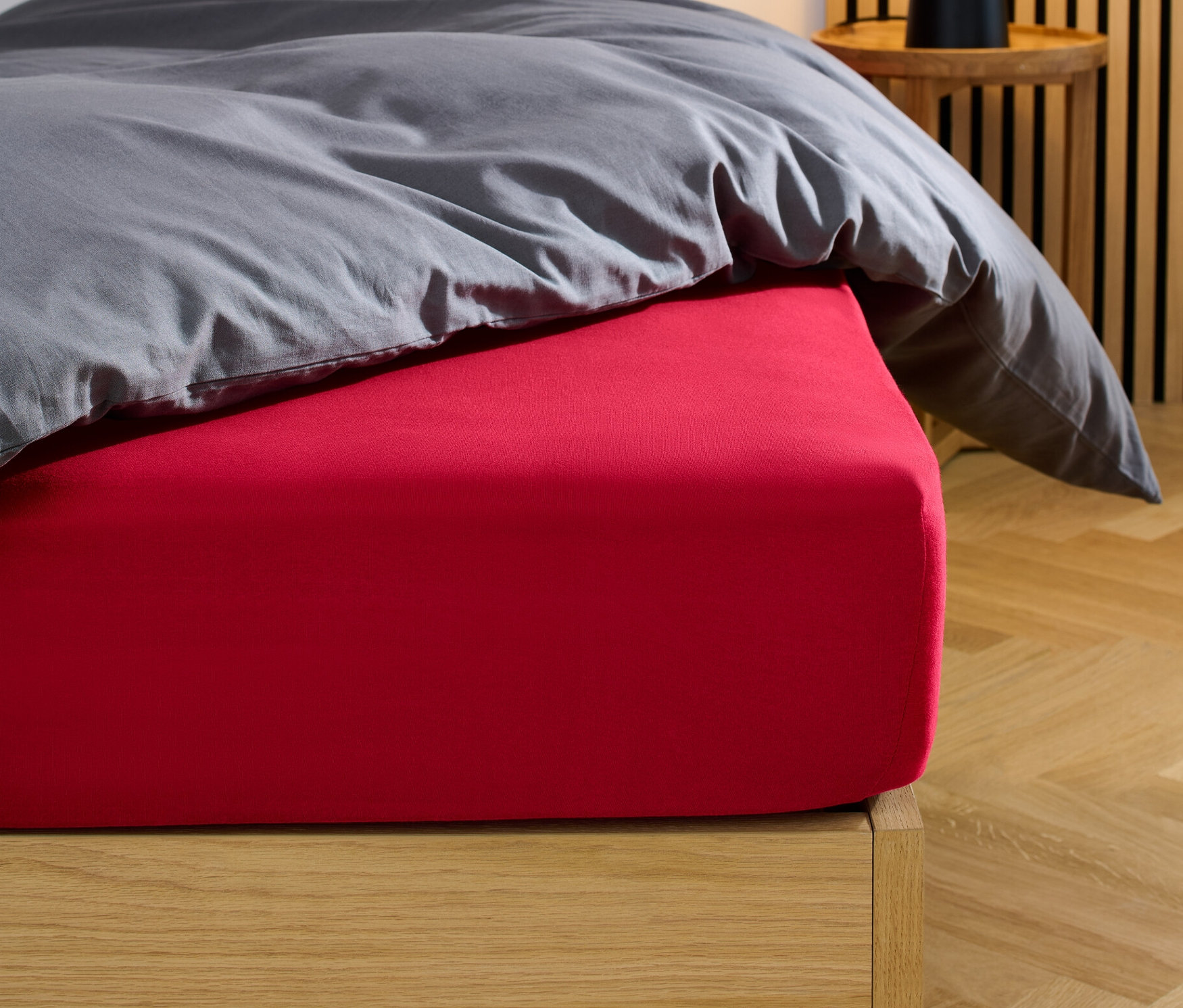Drap-housse en jersey rouge sur un lit avec une couette et un oreiller gris.