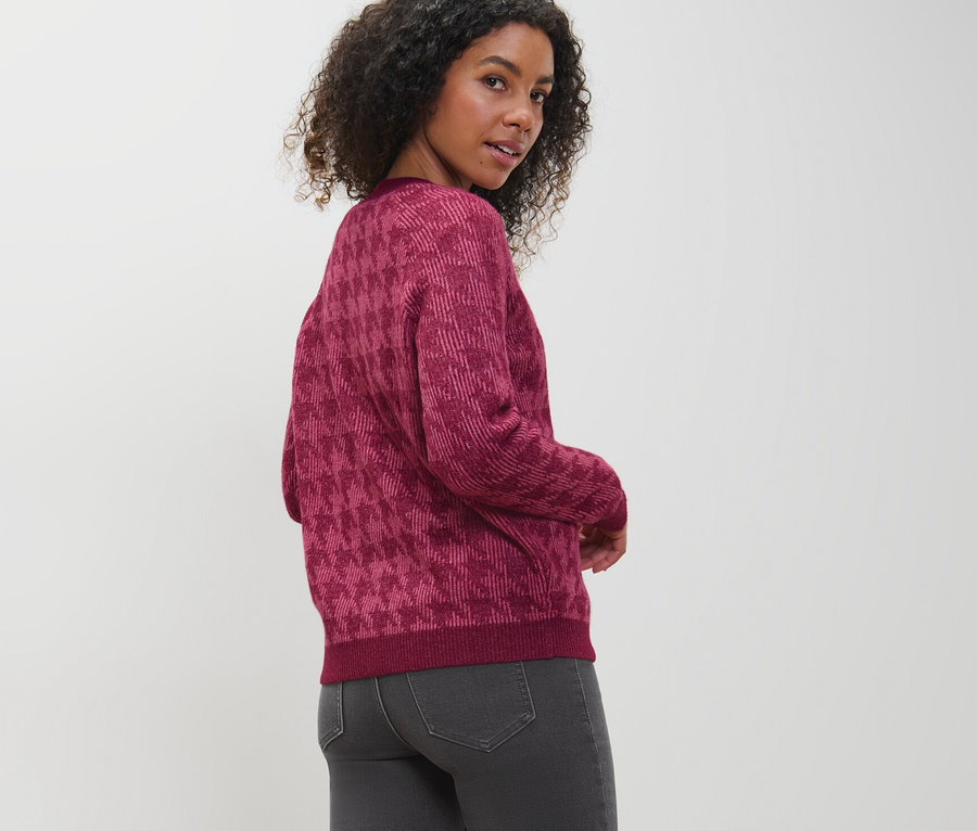 Une femme regarde par-dessus son épaule et porte un cardigan en grosse maille à jacquard pied-de-poule.