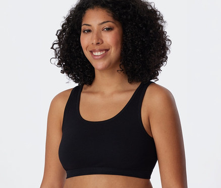 Femme souriante aux cheveux bouclés foncés portant une brassière SCHIESSER noire.