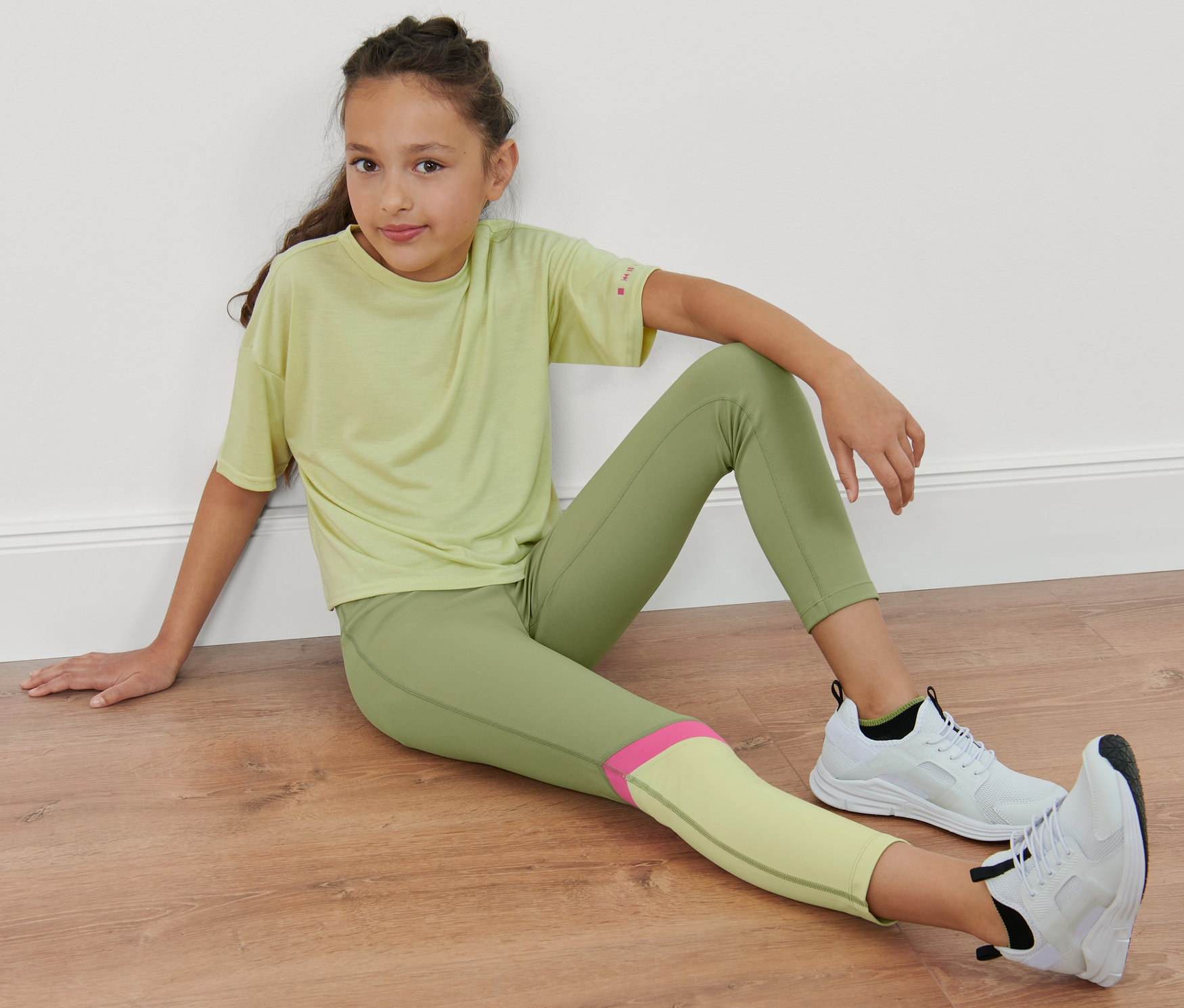 Fille assise par terre portant un legging de sport enfant vert.
