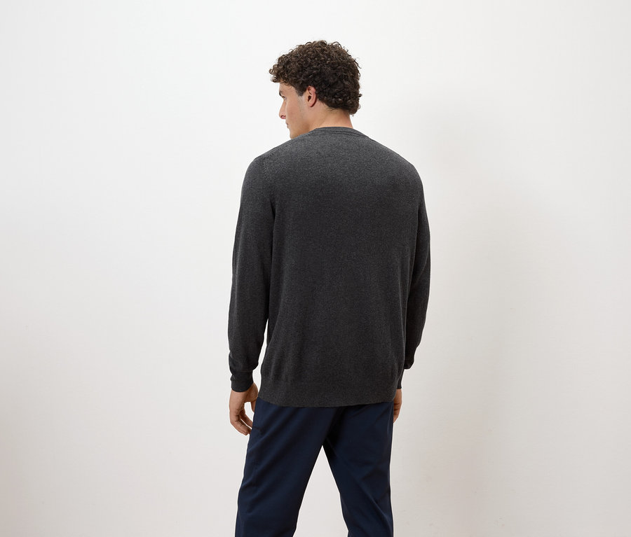 Un homme aux cheveux bouclés, vu de dos, portant un pull gris et un pantalon bleu marine.