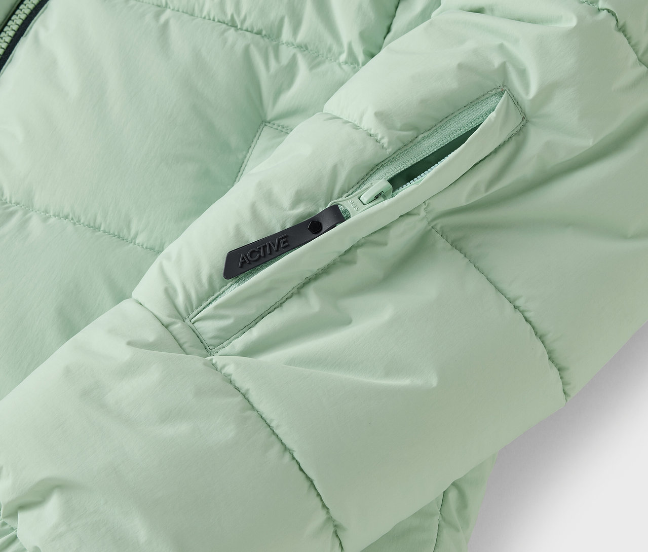 Détail d'une doudoune vert clair avec une poche zippée.