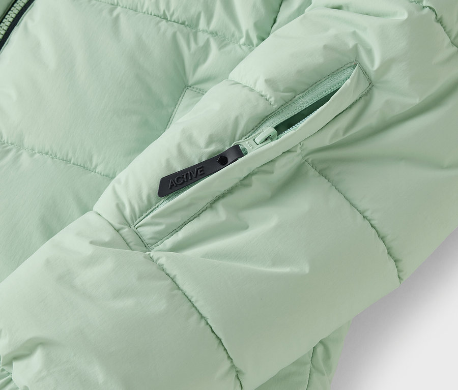 Détail d'une doudoune vert clair avec une poche zippée.