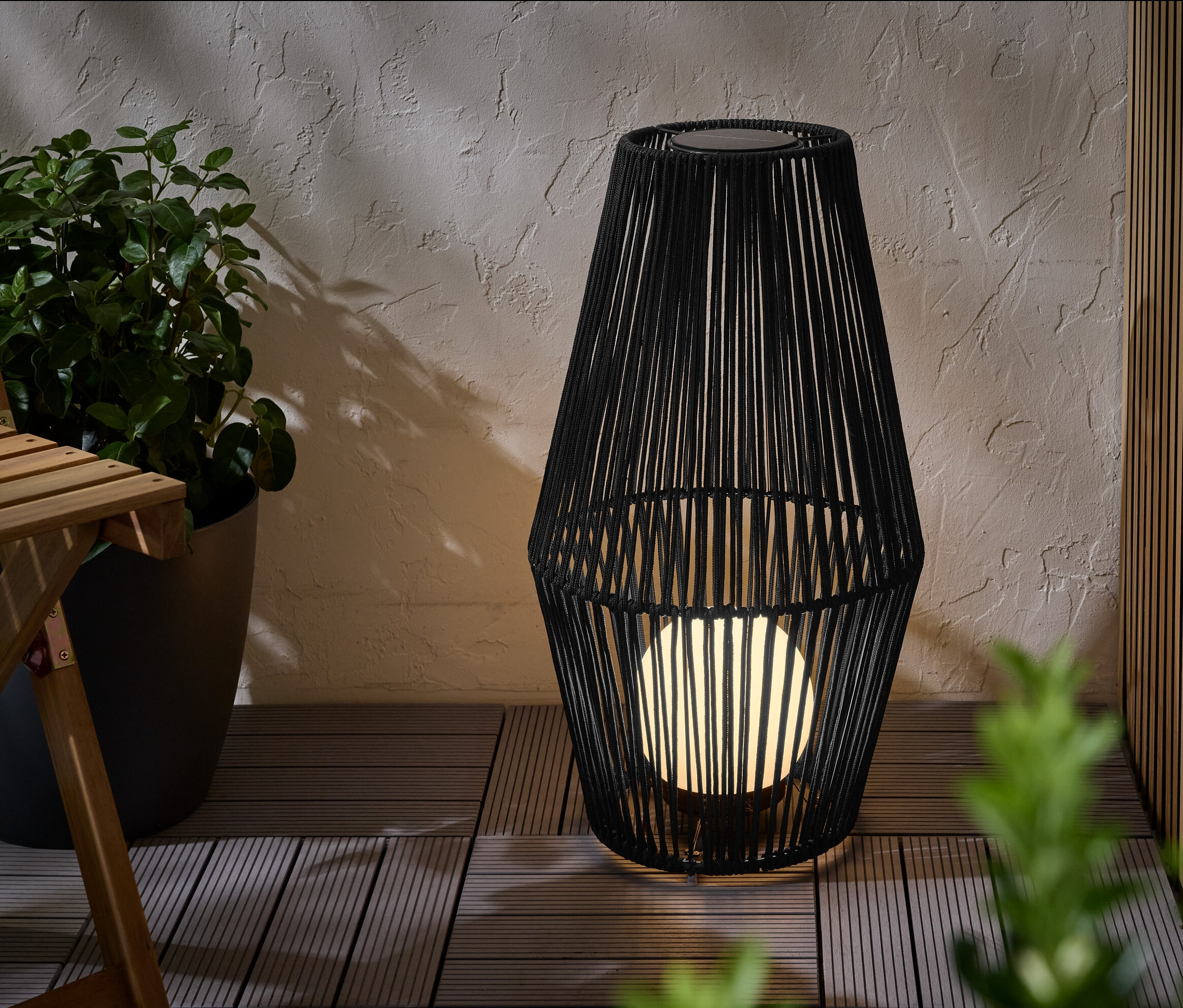 Une grande lanterne solaire avec ruban en tissu est posée sur une terrasse.