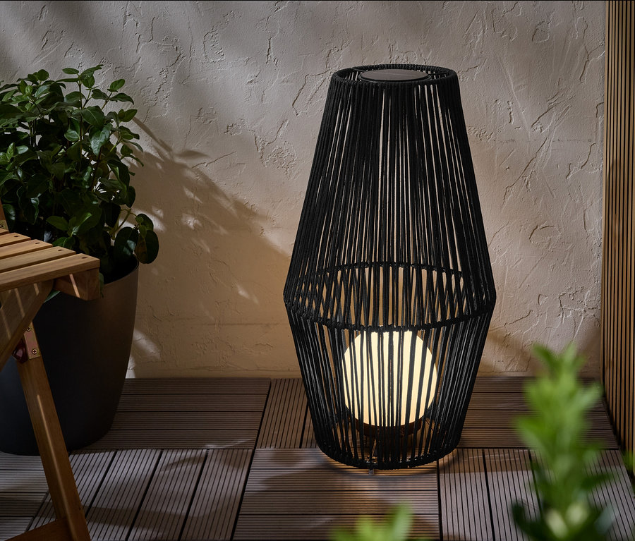 Une grande lanterne solaire avec ruban en tissu est posée sur une terrasse.