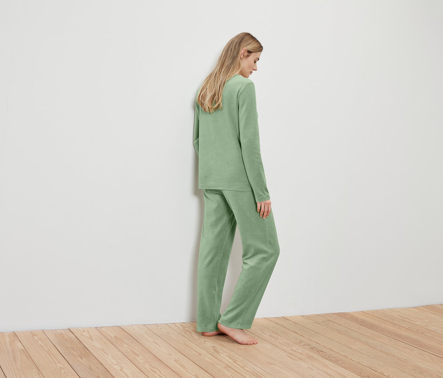 Une femme blonde en pyjama vert clair, dos au mur.