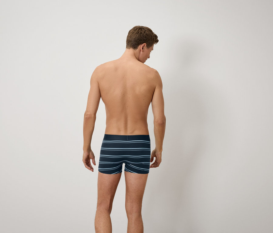 Un homme, dos à la caméra, porte un boxer bleu rayé.