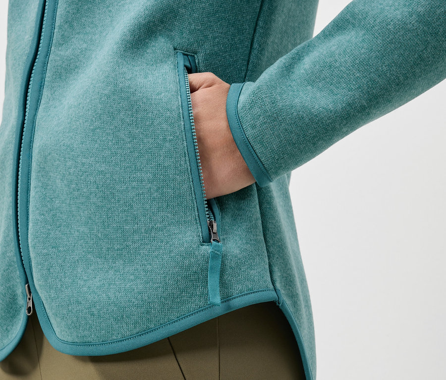 Gros plan d'une veste en polaire turquoise avec une main dans la poche.