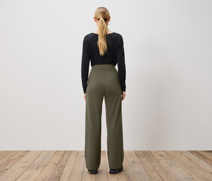 Une femme vue de dos avec une queue de cheval porte un t-shirt noir à manches longues et un pantalon vert olive.